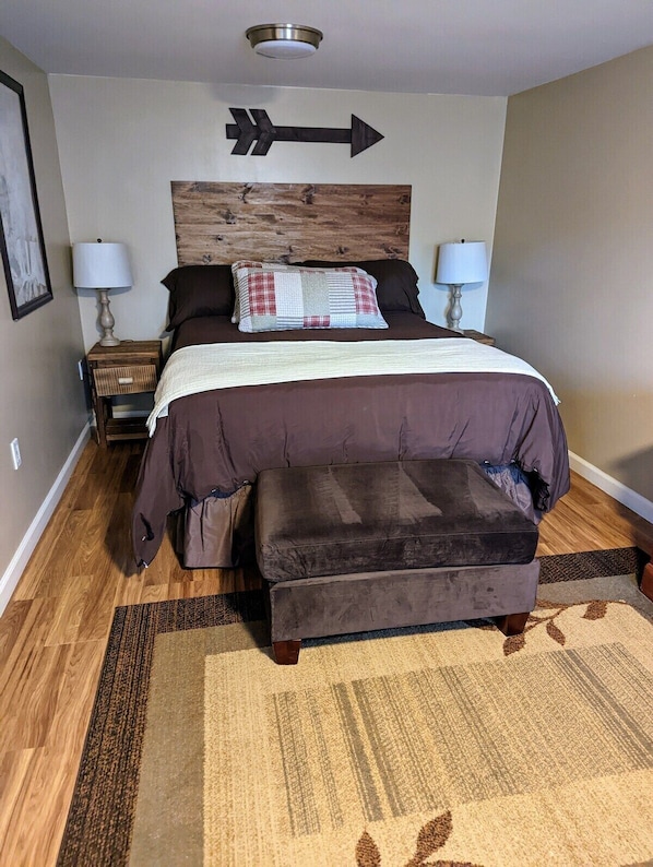 Ein Schlafzimmer mit einem Bett, Nachttischen, einem Pfeilschild an der Wand und einem gemusterten Teppich.