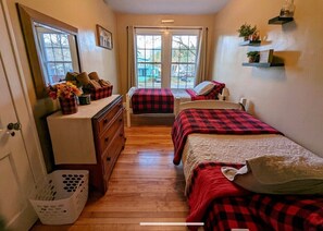 Ein Schlafzimmer mit zwei Betten, einem Schminktisch, einem Korb und einem Fenster mit Blick ins Freie.