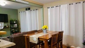 A dining area with a wooden table and chairs, a vase with yellow flowers, and white curtains.