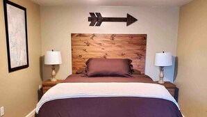 A bedroom with a large bed, two bedside lamps, a wooden headboard, and a directional arrow sign on the wall. - Robin's Nest Queen Suite with Private Bath (Saranac Lake)