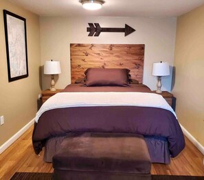 Une chambre à coucher avec un grand lit, deux lampes de chevet, une tête de lit en bois et un panneau mural indiquant la direction.