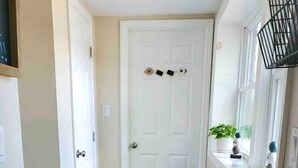 A hallway with a wooden floor, a white door, a small rug, and a window with a plant. - Robin's Nest Queen Suite with Private Bath (Saranac Lake)