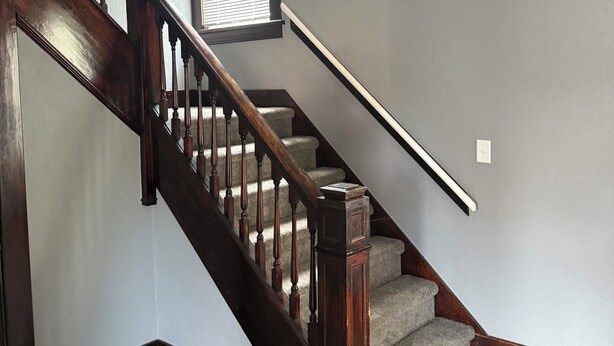 A wooden staircase with a handrail, carpeted steps, and a window with blinds. - Newly Renovated Spacious Home! Minutes from cedar point and downtown Sandusky! (Sandusky)