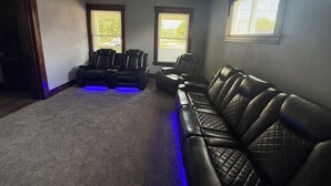 A room with a ceiling fan, two windows with blinds, a dark-colored leather sofa, and a massage chair with blue LED lighting. - Newly Renovated Spacious Home! Minutes from cedar point and downtown Sandusky! (Sandusky)