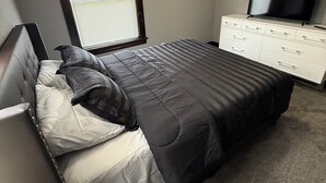A bedroom with a bed, a dresser, a TV, and a window with blinds. - Newly Renovated Spacious Home! Minutes from cedar point and downtown Sandusky! (Sandusky)