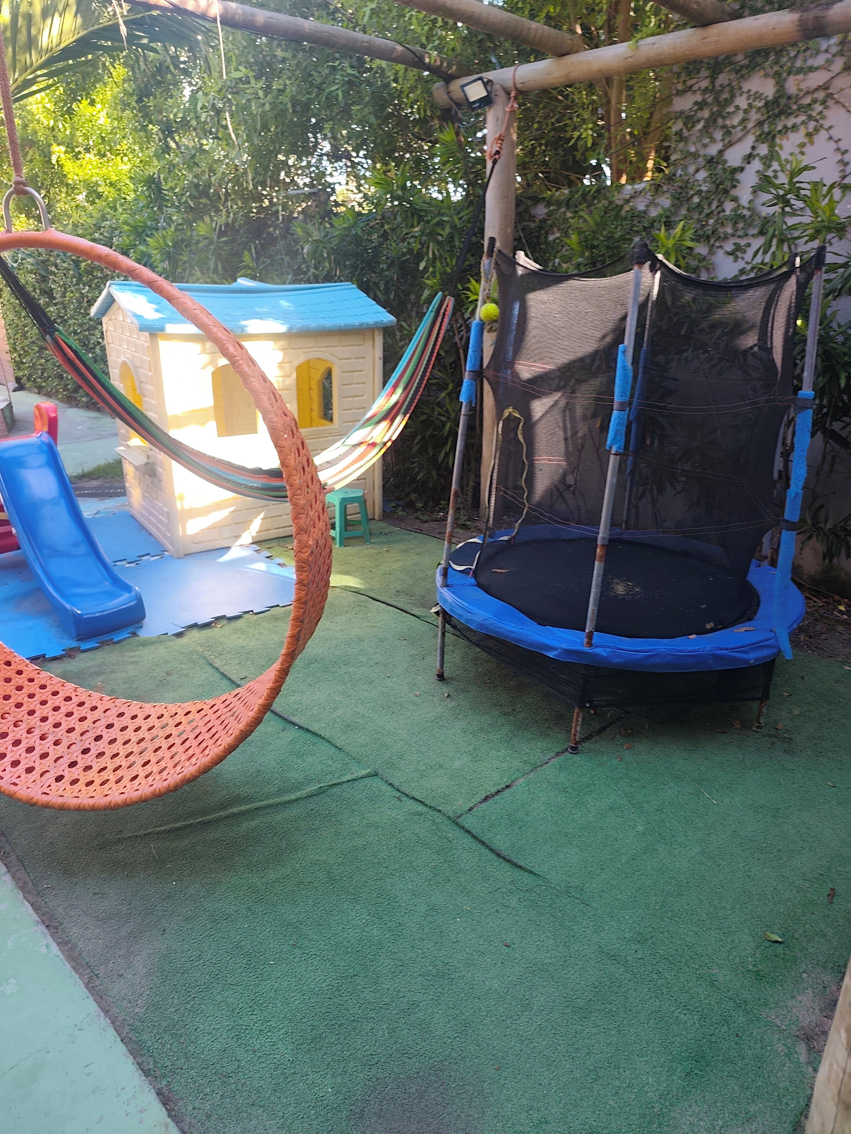 A trampoline, a hanging hammock, and a small playhouse in a backyard.