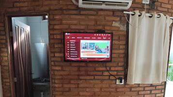 Habitación con pared de ladrillo, un televisor montado que muestra un menú, una mesa de masajes con toallas y un equipo de aire acondicionado.