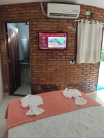 Habitación con pared de ladrillo, un televisor montado que muestra un menú, una mesa de masajes con toallas y un equipo de aire acondicionado.