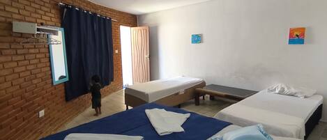 A hotel room with two beds, a brick wall, a window with curtains, and a small painting on the wall.