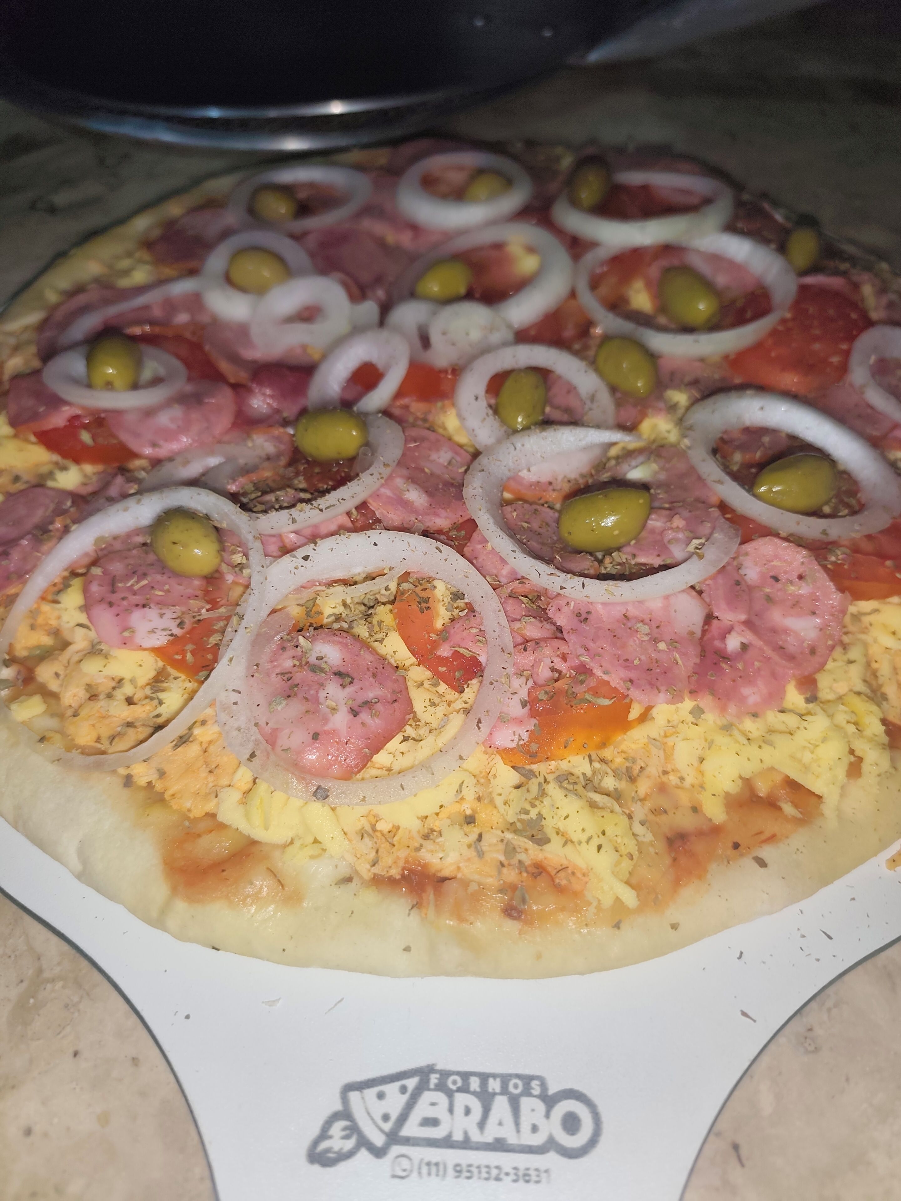 A pizza with toppings including ham, tomatoes, onions, and olives.