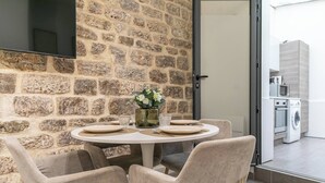 Un coin repas agrémenté d’un mur en pierre, d’une table ronde dressée pour quatre personnes et d’une vue sur la cuisine.