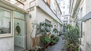 Une ruelle étroite, bordée de plantes en pot, avec une porte sur le côté gauche.