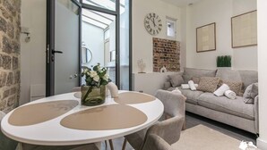 Un salon chaleureux avec un canapé gris, une table ronde ornée d’un vase de fleurs et un mur en briques qui apporte une touche d’originalité.