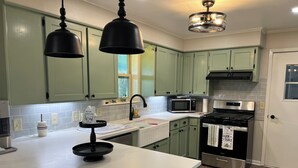 A kitchen with green cabinets, a white countertop, a black stove, a microwave, and pendant lights. - Windy Hill Farmhouse in Caldwell (Caldwell)