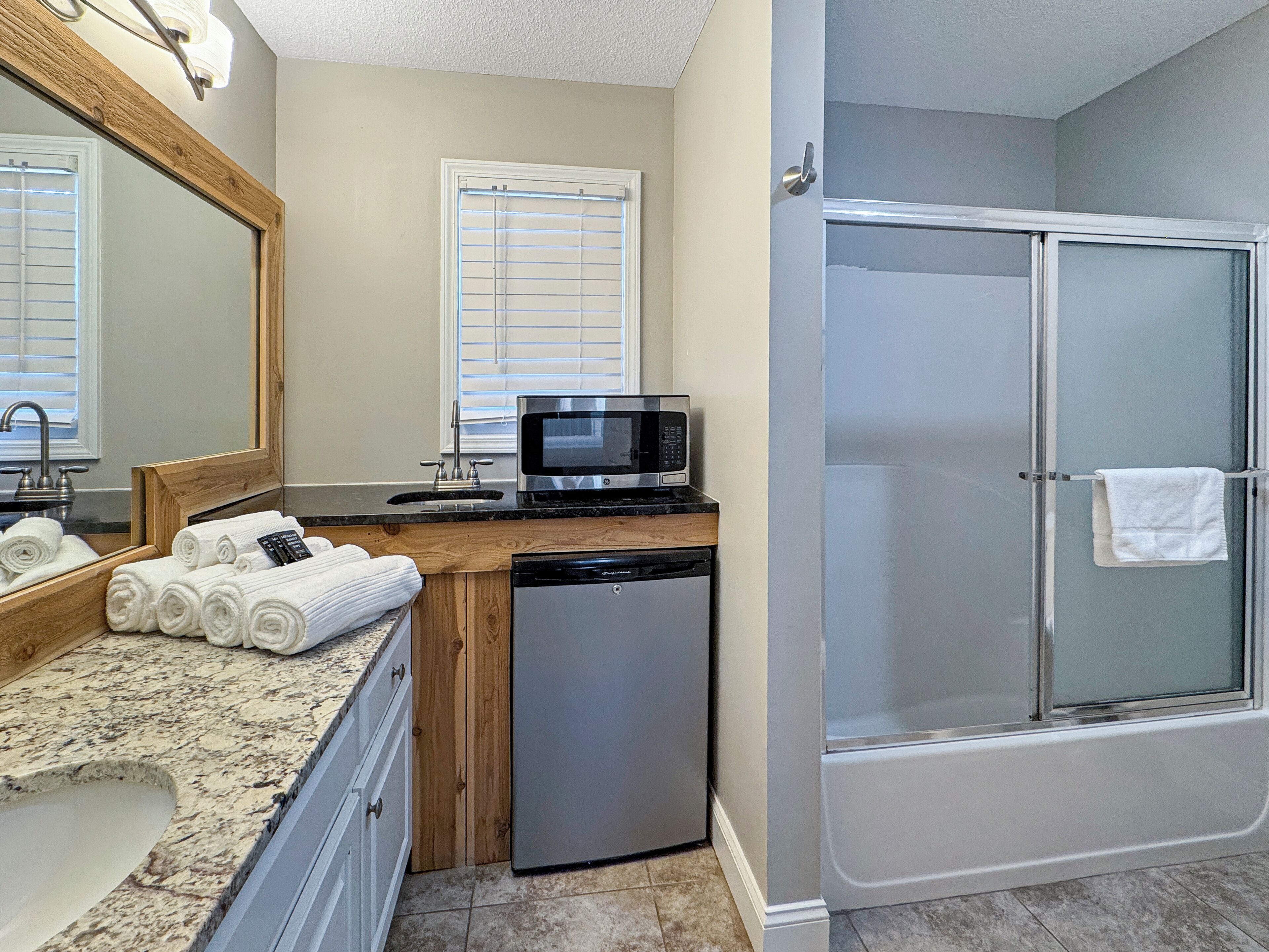 A bathroom with a sink, mirror, towel rack, and a shower area.