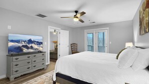 A bedroom with a bed, a ceiling fan, a dresser, a television, and a door leading to another room.