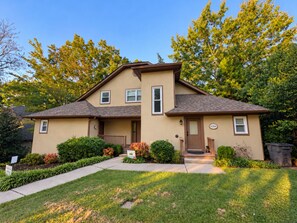 A two-story residential house with a front porch, a small garden, and a well-maintained lawn.