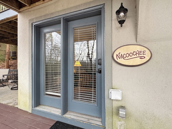 A building entrance with a double door, a wall-mounted sign reading 'NACOCHEE,' and a small electrical box.
