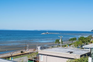 A coastal view with a pier extending into the water, a beach, and a building with a flat roof in the foreground. - Oceanfront - Steps to Pier & Beach - Free Onsite Parking (White Rock)