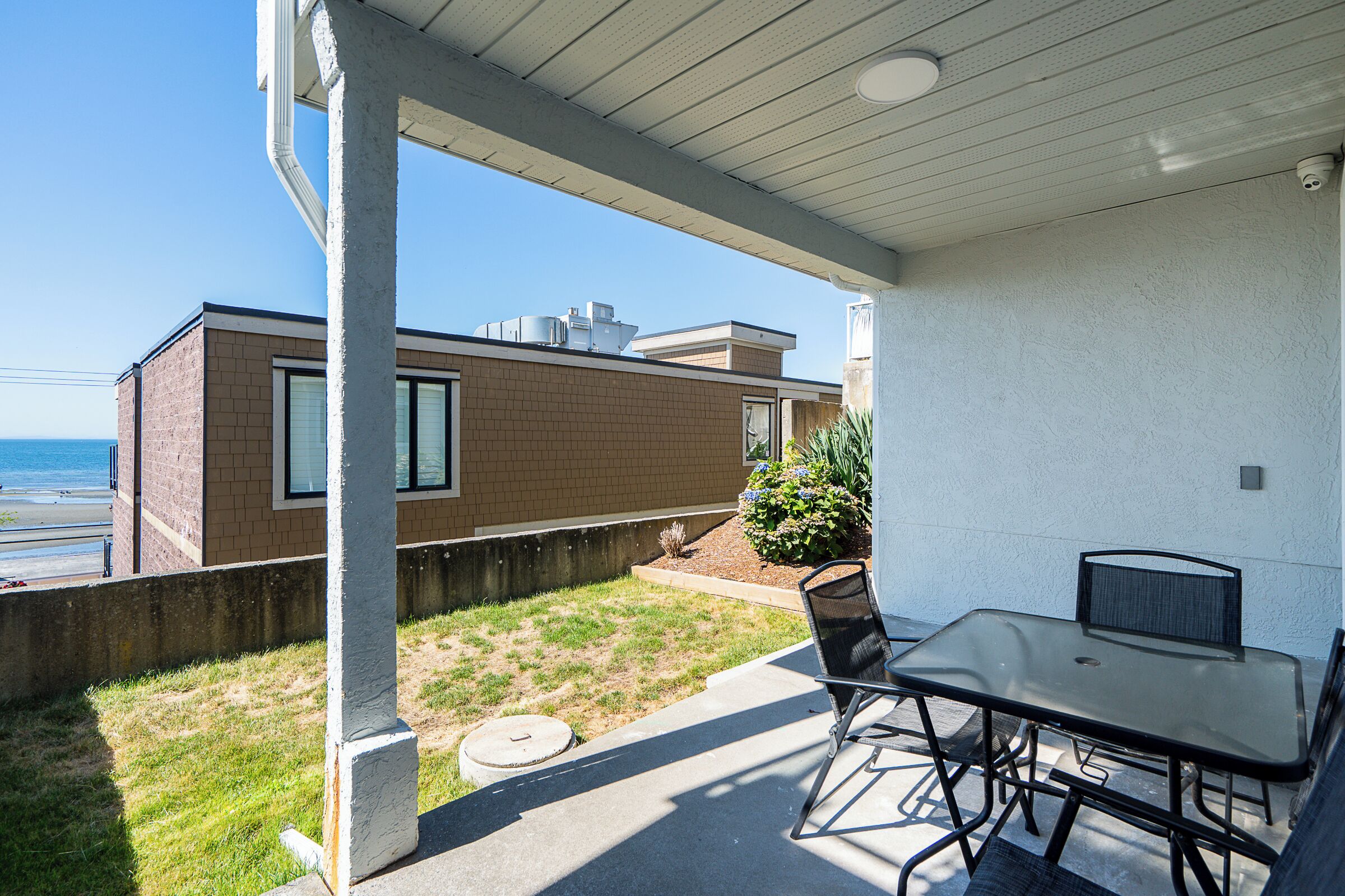 A covered patio with a table and chairs, a view of a building with a brick facade, and a clear sky.