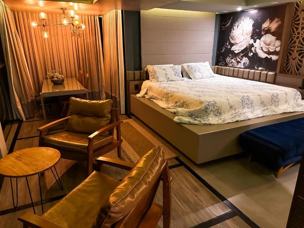 A bedroom with a large bed, a seating area with chairs and a table, and a decorative wall.
