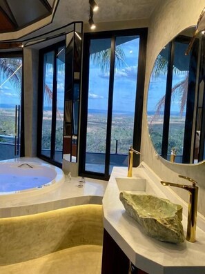 A modern bathroom with a large bathtub, a sink with a unique stone basin, and a large mirror. - Mirante Pousada Boutique (Primavera do Leste)