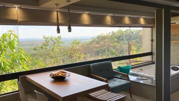 Una habitación moderna con un ventanal grande, una mesa de madera, dos sillas, un sofá pequeño y una bañera.
