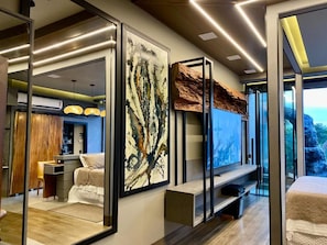 A modern hotel room with a large bed, a seating area, and a large window offering a view of the outdoors. - Mirante Pousada Boutique (Primavera do Leste)