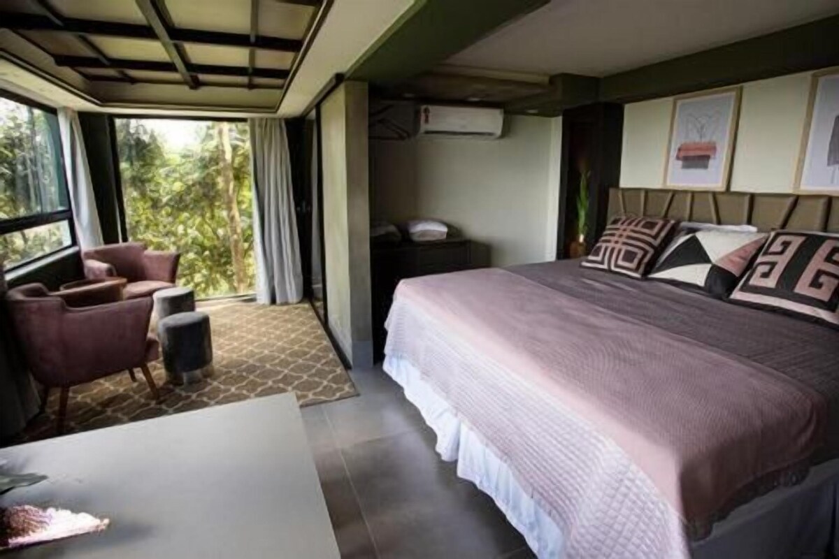 A hotel room with a large bed, a desk, a chair, and a view of the outdoors.