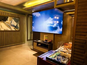 A modern living room with a flat-screen TV mounted on the wall, a wooden entertainment unit below, and a glass-topped coffee table with wine glasses. - Mirante Pousada Boutique (Primavera do Leste)