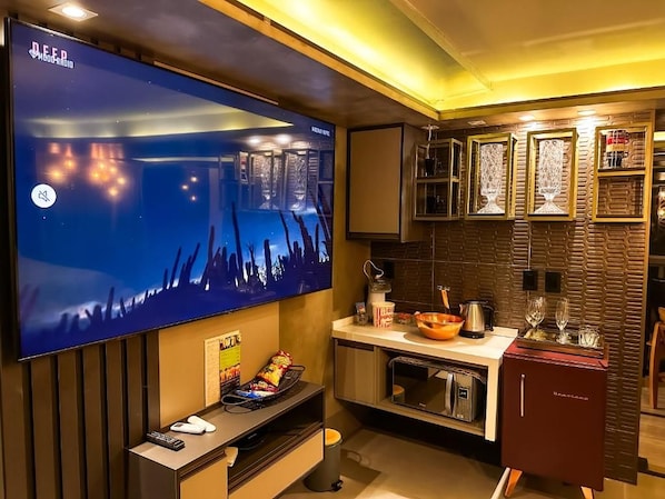 A modern kitchen with a flat-screen TV, built-in microwave, and a compact refrigerator.