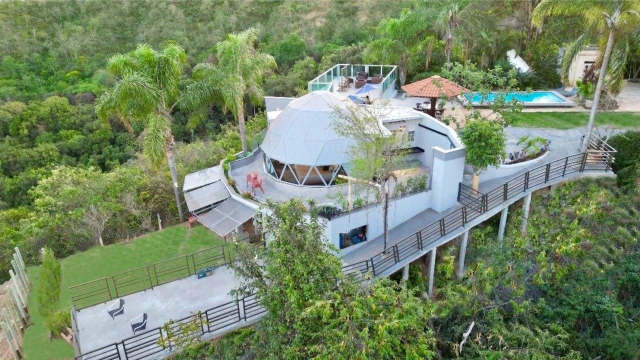 A modern house with a unique dome-shaped roof, surrounded by lush greenery and a swimming pool.