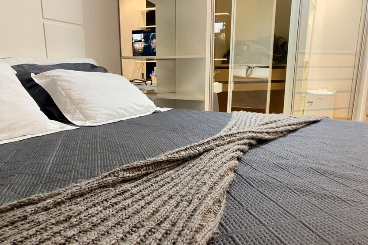 A bed with a grey textured bedspread and a beige knitted throw.