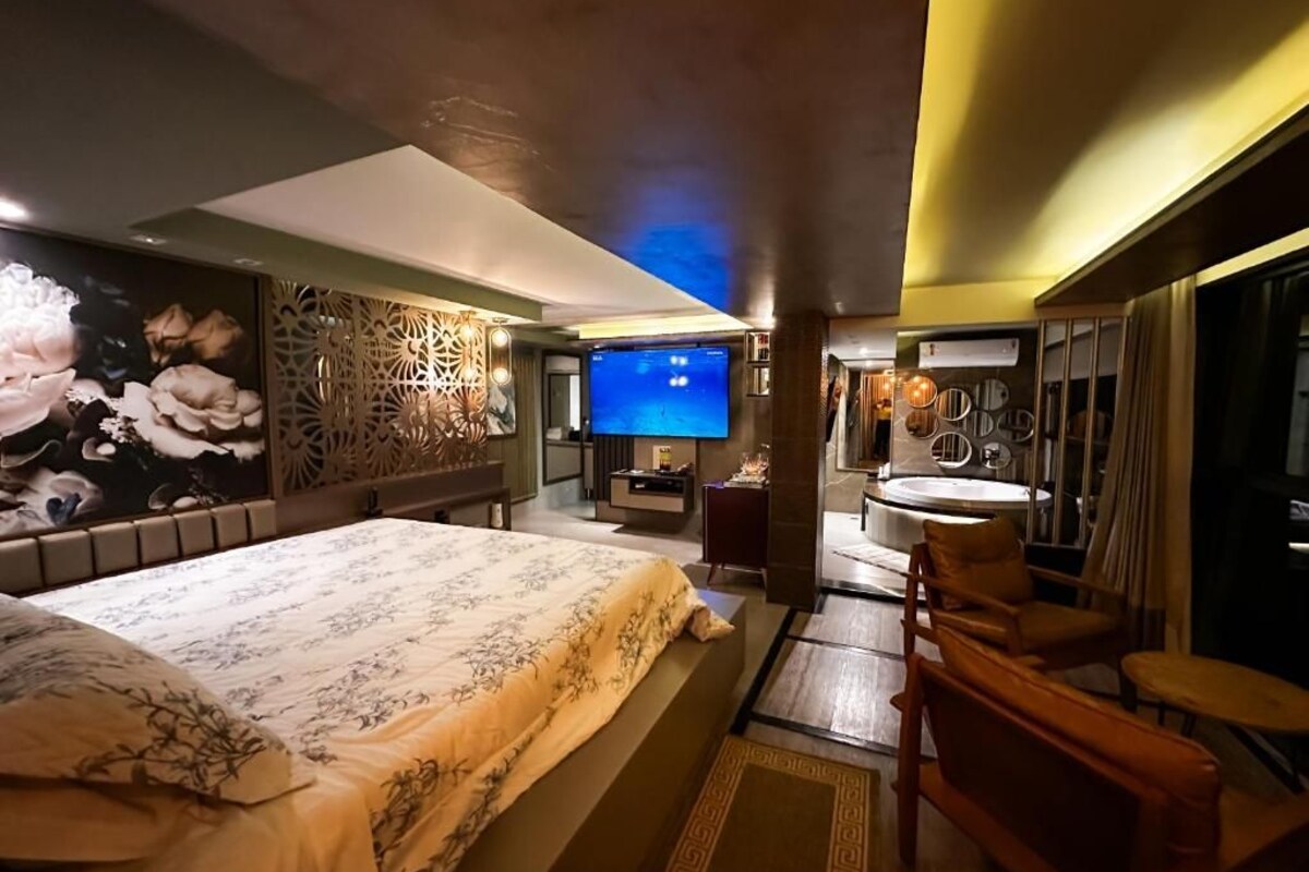 A hotel room with a large bed, a TV, a bathroom, and a seating area.