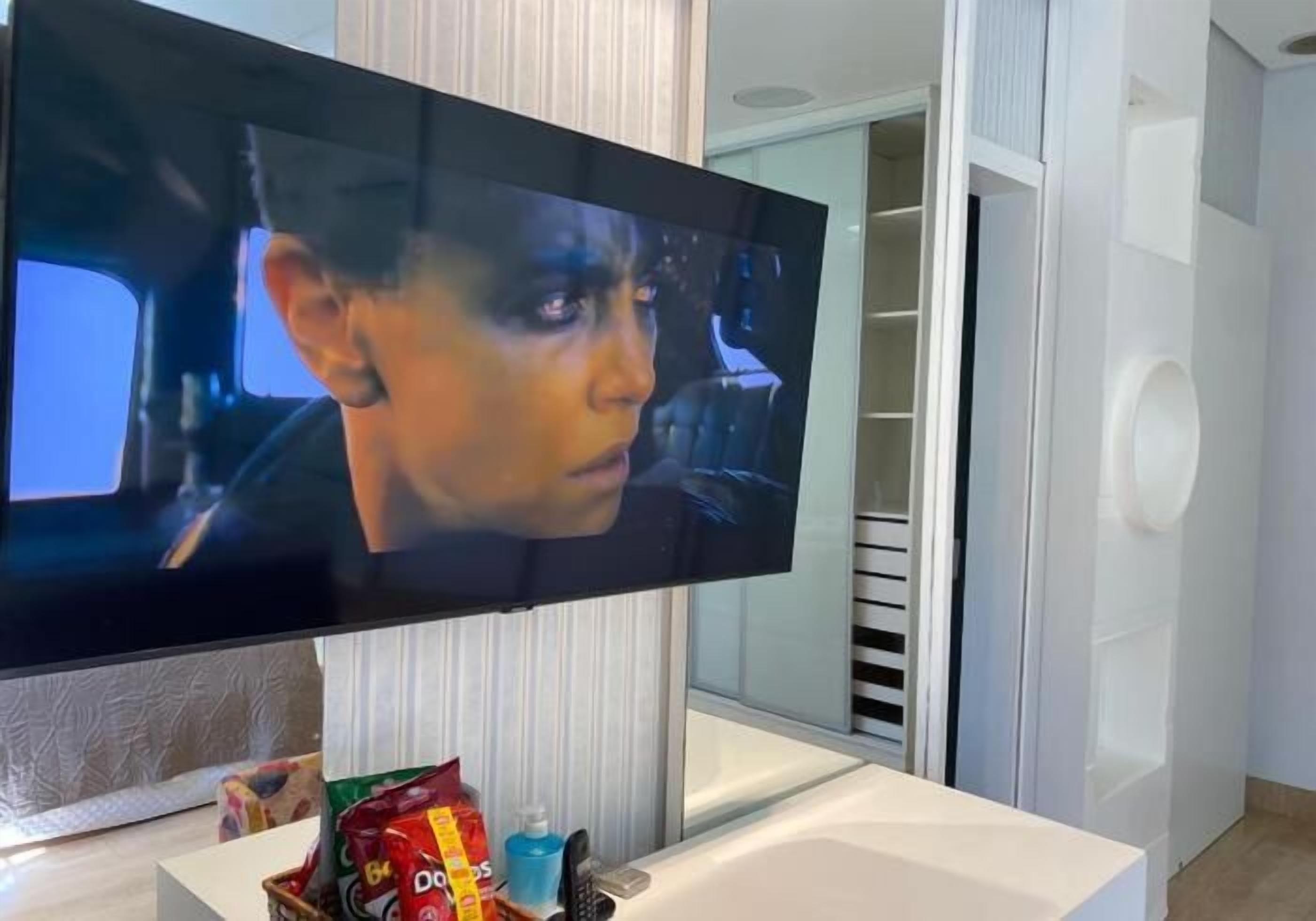 A flat-screen TV mounted on a white wall, with snacks on a small table in front.