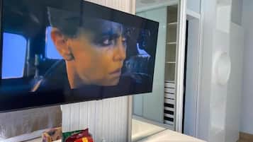 A flat-screen TV mounted on a white wall, with snacks on a small table in front.
