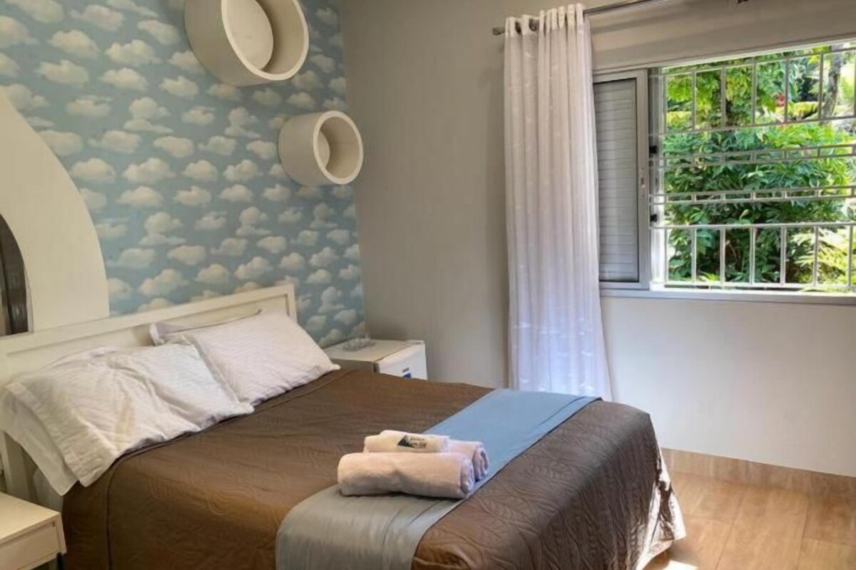 A bedroom with a bed, a nightstand, a window with curtains, and a wall with a cloud pattern.