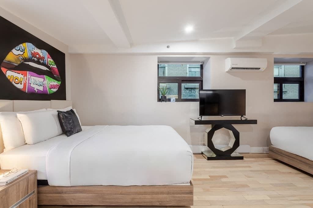 A modern bedroom with a large bed, a TV on a stand, and a window with a view of the outside.