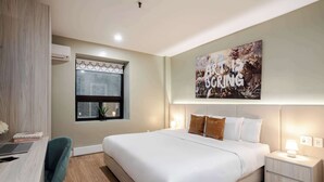 Una habitación de hotel moderna con una cama grande, un escritorio con una computadora portátil, una ventana con persianas, un aire acondicionado montado en la pared y un cartel motivacional.