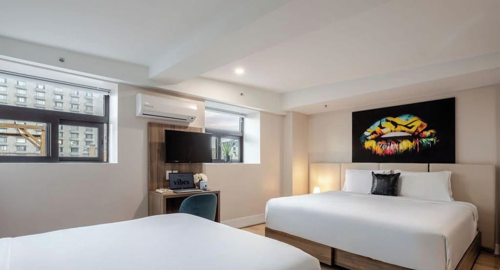 Une chambre d’hôtel avec deux lits, un bureau, une télévision et une grande fenêtre.