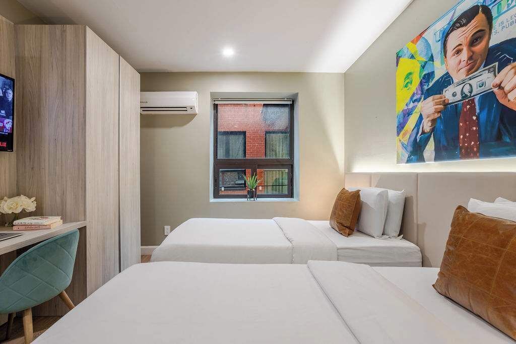 Een hotelkamer met twee bedden, een bureau met stoel, een televisie en een raam met uitzicht op een bakstenen gebouw.