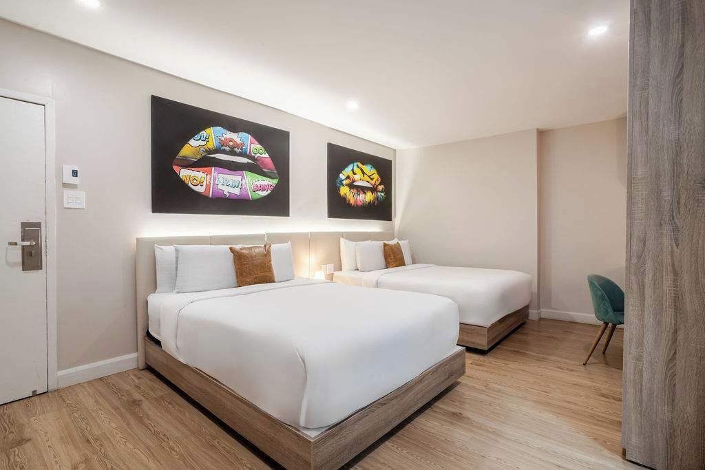 A hotel room with two beds, a wooden floor, and two wall art pieces.