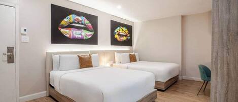 A hotel room with two beds, a wooden floor, and two wall art pieces.