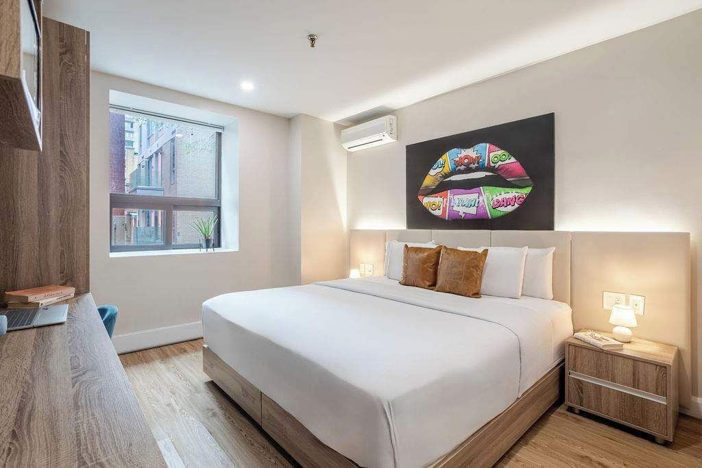 A modern hotel room with a large bed, a desk, a nightstand, and a window with a city view.