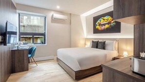 Ein modernes Hotelzimmer mit Bett, Schreibtisch und Fenster mit Blick auf eine Skyline.