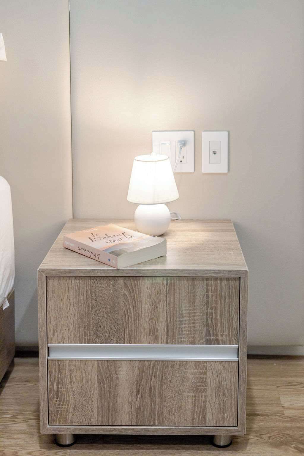 A wooden nightstand with a white lamp and a book.