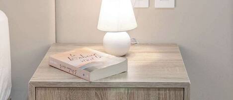 A wooden nightstand with a white lamp and a book.