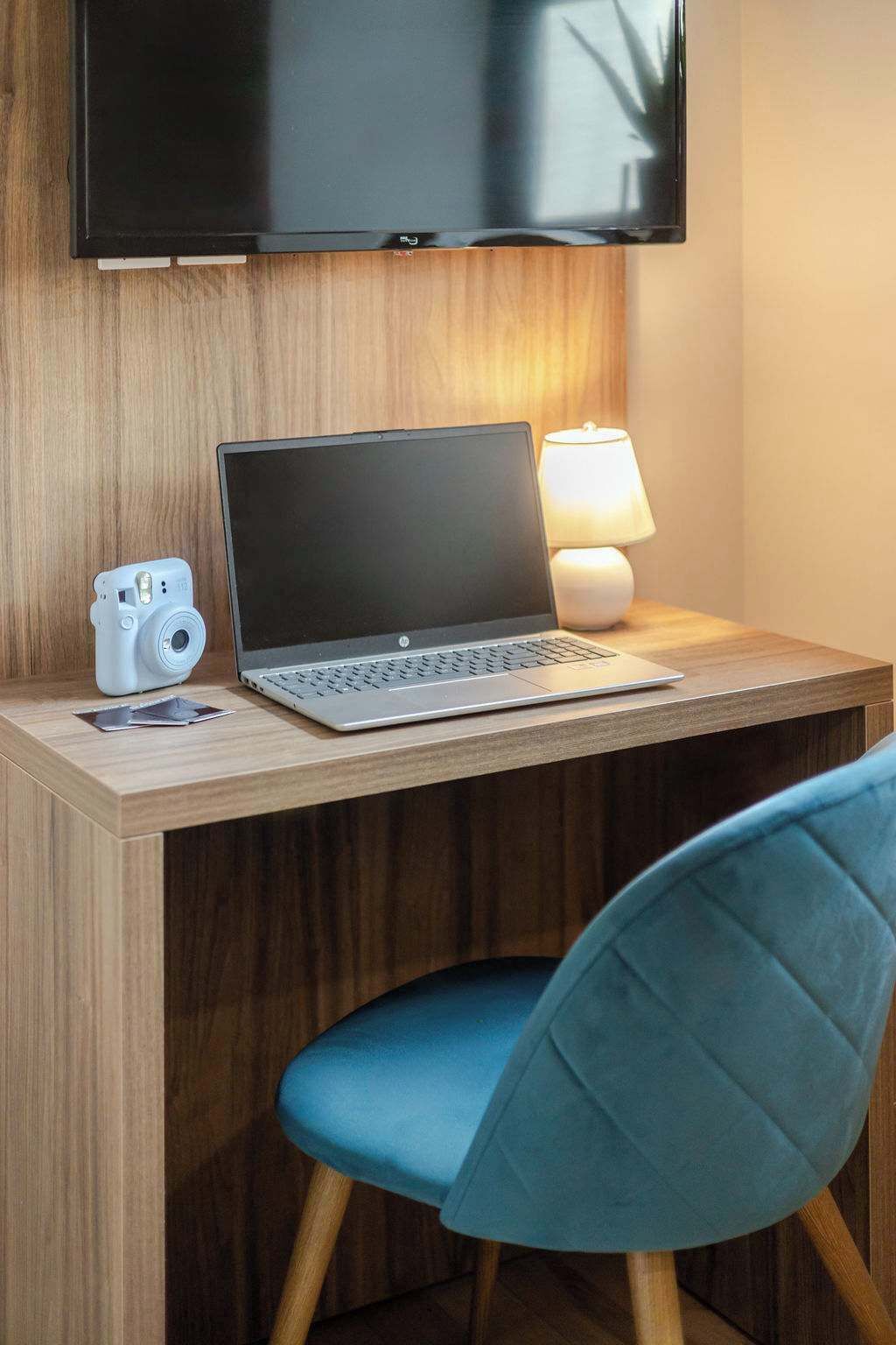 A hotel room with a wooden desk, a laptop, a camera, and a lamp.