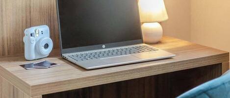 A hotel room with a wooden desk, a laptop, a camera, and a lamp.