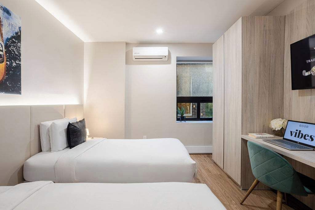 Ein Hotelzimmer mit zwei Betten, einem Schreibtisch mit einem Laptop, einer Klimaanlage und einem Fenster mit Blick.
